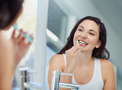 Woman brushing teeth in front of mirror