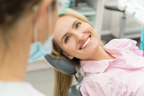 Smiling woman leaning back in dental chair looking up at dentist