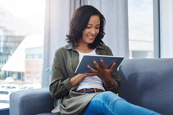 A woman smiling and sitting on a sofa while scheduling an appointment with her Periodontist.