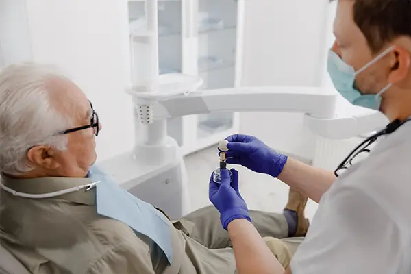 A dentist explains the signs of peri-implantitis to an older patient with implant tooth model.