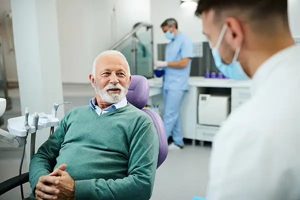 An older male patient sitting in a dental chair and consulting with a Periodontist in a modern clinic.