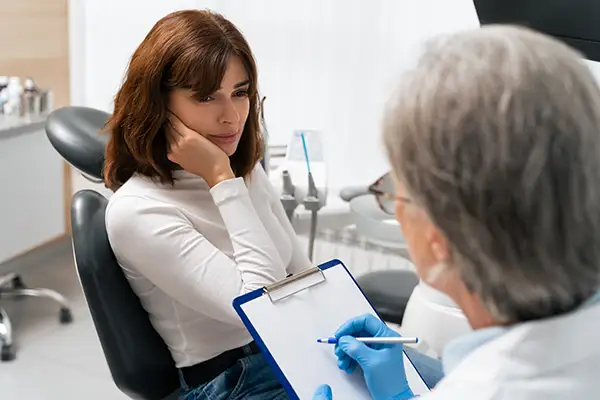 Female patient consulting with a dentist about severe tooth sensitivity during a dental appointment in a clinic.