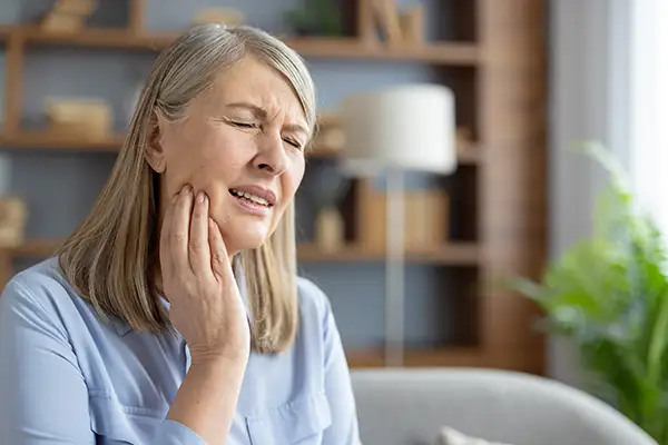 Elderly woman sitting at home, holding her jaw and grimacing in pain, from a cold sore.