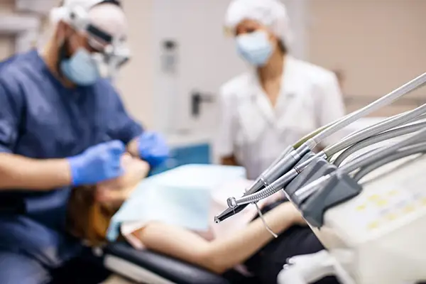 A close-up view of dental tools with a dentist and assistant working on a patient in the background during gum reshaping procedure.